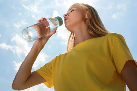 Persona bebiendo agua bajo el sol para evitar el golpe de calor en verano.